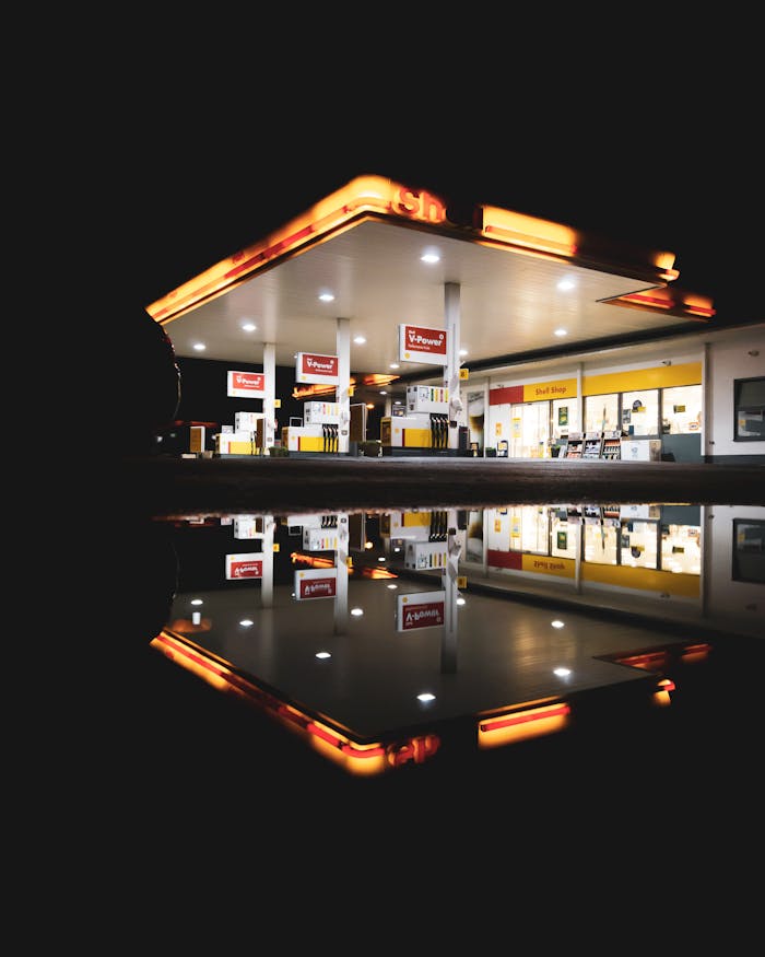 A gas station lit up at night with a vivid reflection in a puddle, creating a striking visual contrast.