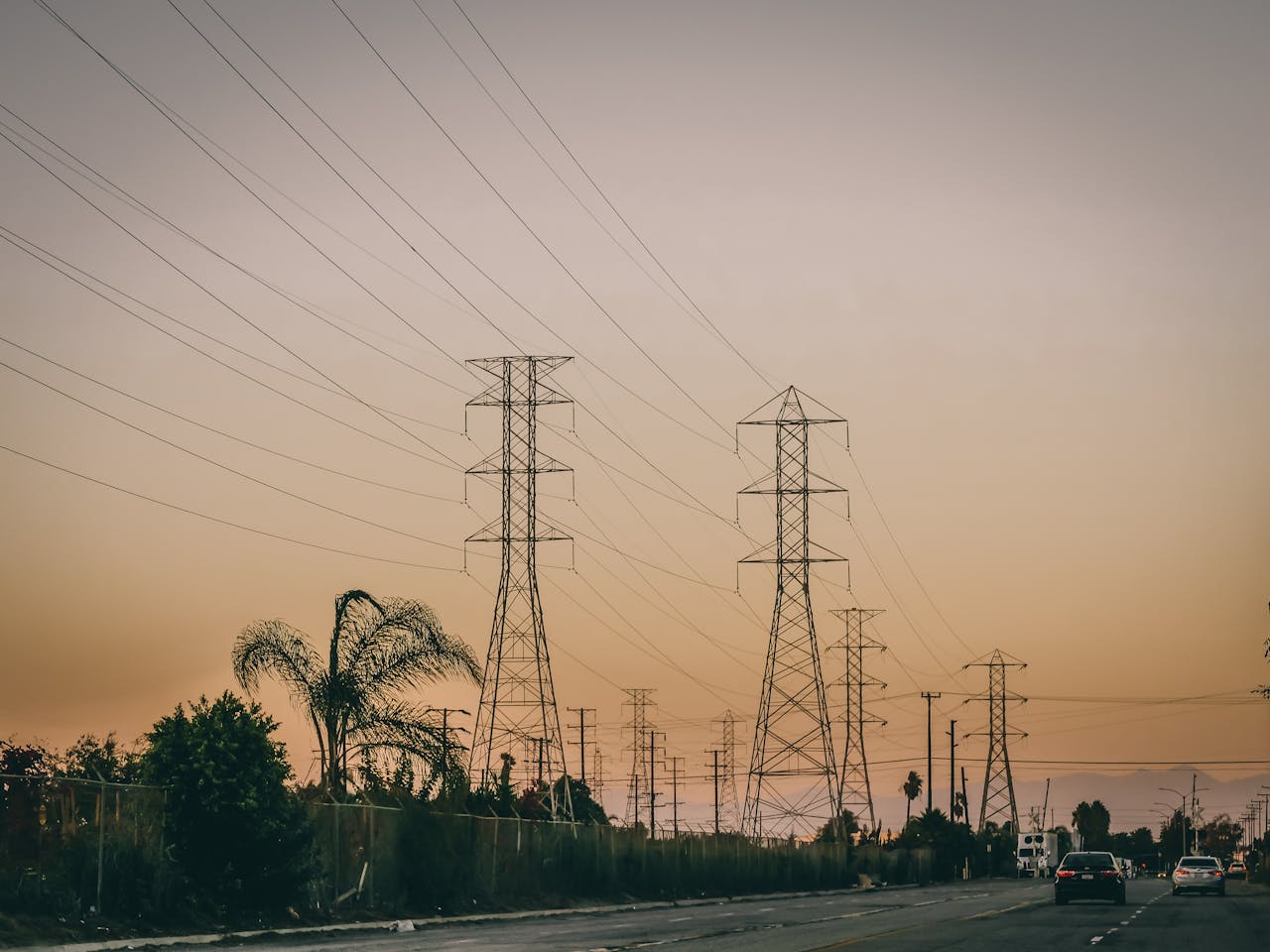 Transmission towers and road under a sunset sky symbolizing energy distribution.